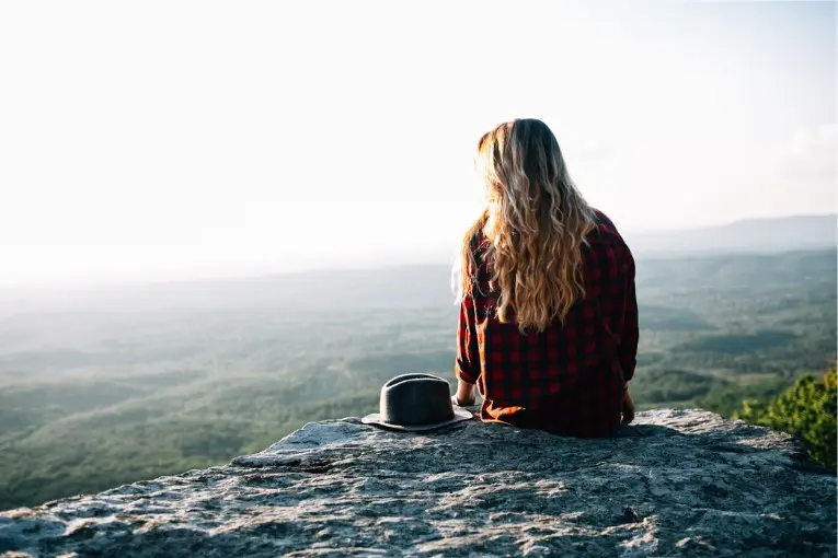 person wearing plaid shirt while sitting on the top of a boulder