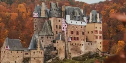 brown castle with gray roof on mountain surrounded by autumn leaves