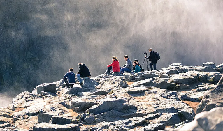 Group of adventurers resting on rocks, admiring and photographing the beauty of a mountain mist