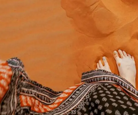 Woman stands barefooted on sand dune