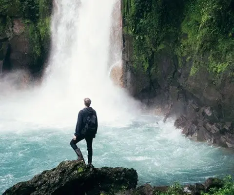 Man standing on edge of rock looking at waterfall