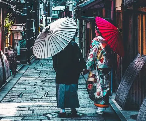 two people walking down a street in kyoto, japan