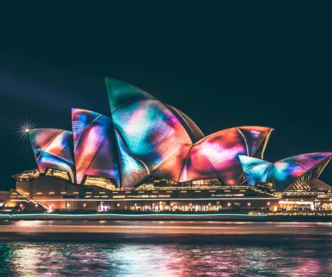 Sydney Opera House lit up in rainbow at night on the harbour