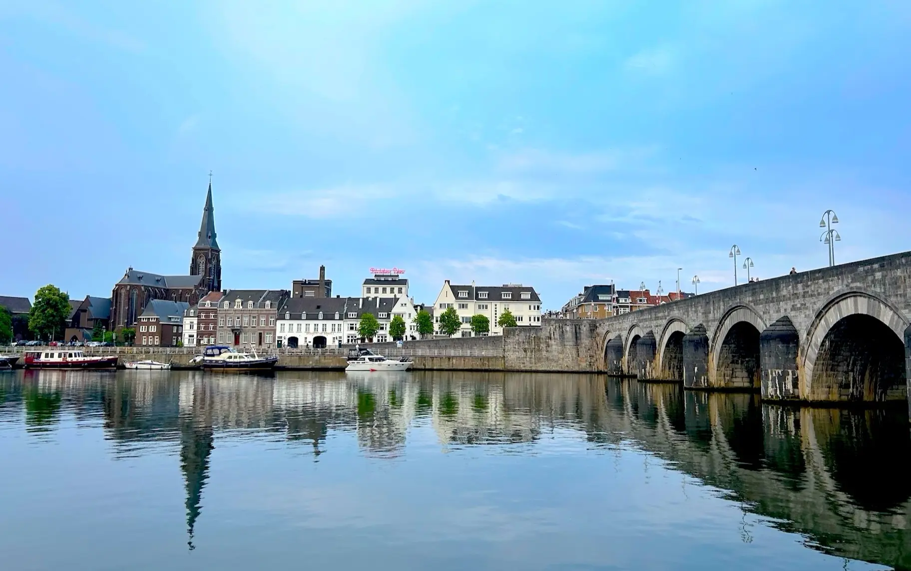 A wide view of a city across a calm river, featuring the Sint Servaasbrug, a historic stone arch bridge in Maastricht, Netherlands