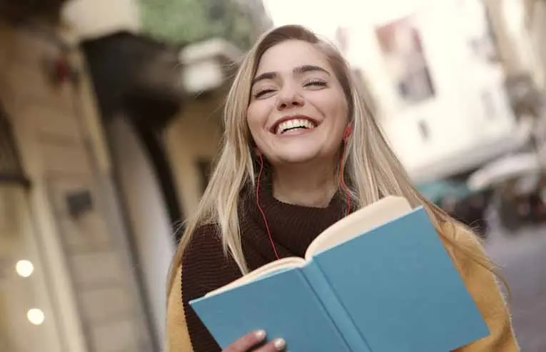 student smiling while reading a book and listening to music 